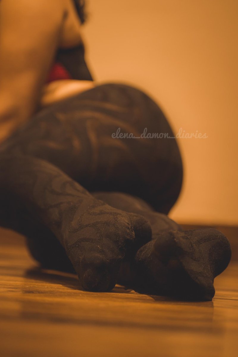 Blurred close-up of feet in dark pantyhose on a wooden floor in warm orange light