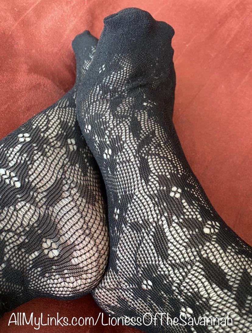 Feet crossed in black floral lace socks on a red blanket