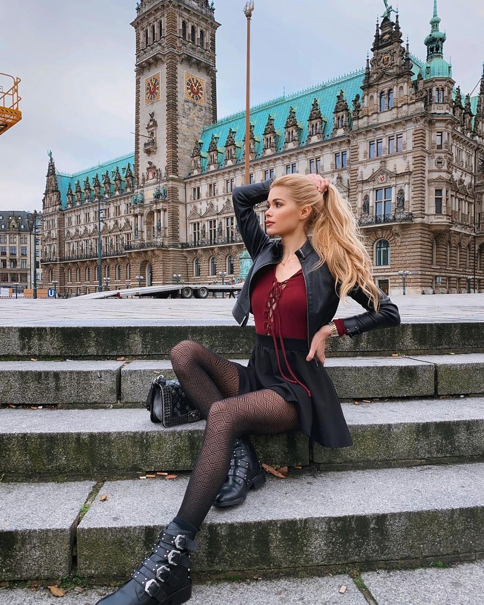 Blonde in a leather jacket and red top sitting on stone stairs in fishnet tights and black boots