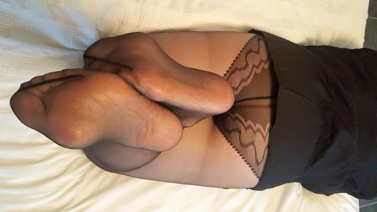 Soles in sheer black pantyhose pushed forward on a white bed with a lace-pattern pantyhose top