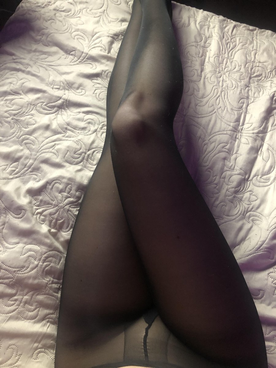 Legs in sheer black pantyhose with a visible seam on lilac patterned bedding