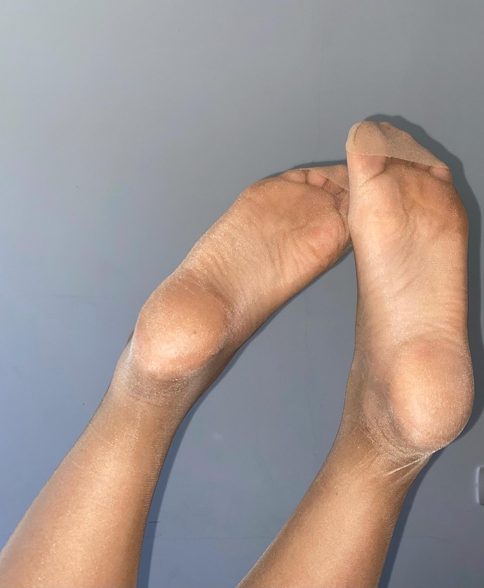 Soles in tan pantyhose crossed in the air against a blue-grey wall
