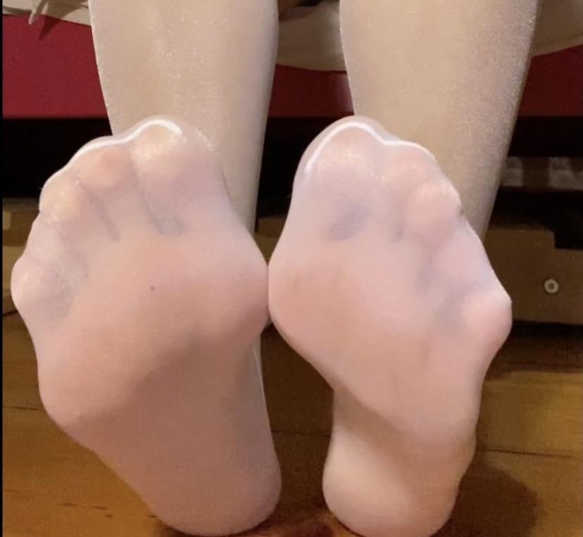 Close-up of soles in glossy pale pink pantyhose on a wooden floor
