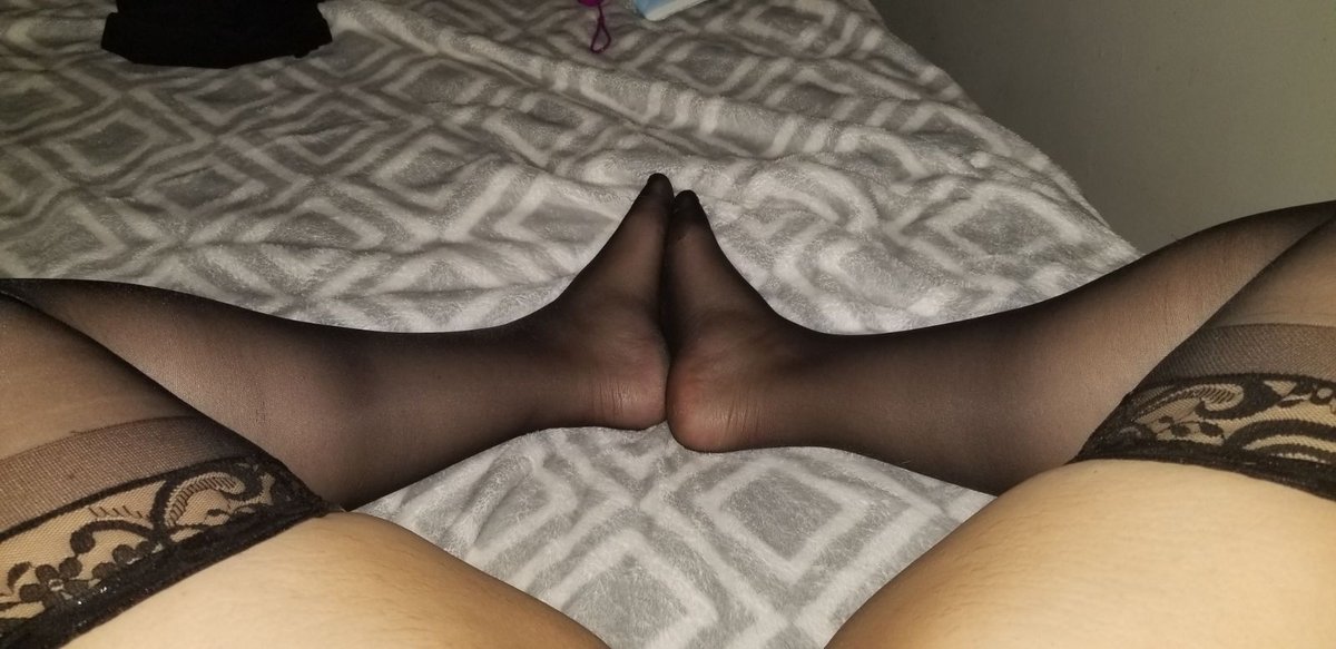 Soles together in sheer black stockings with wide lace tops on a grey geometric blanket