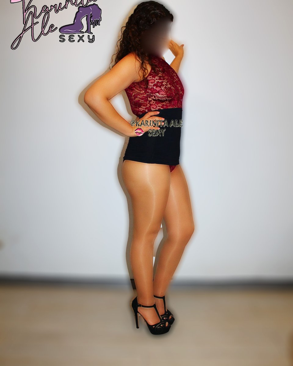 Woman in a red lace top and black skirt standing in shiny nude pantyhose and black platform sandals