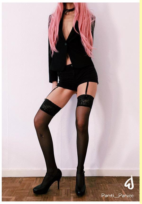 Woman with long pink hair in a black blazer and shorts with garter straps, black lace top stockings with a star pattern and black platform pumps