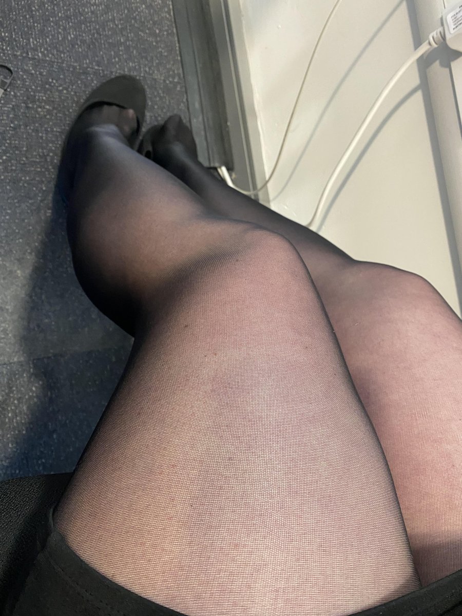 Close-up of legs in sheer black pantyhose crossed with a black pump near a window